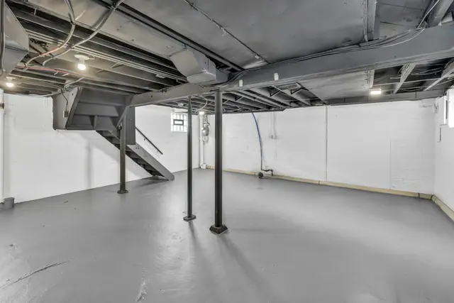 An unfinished basement with exposed joists and support poles