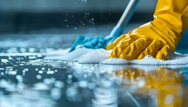 A gloved hand scrubbing a soapy floor