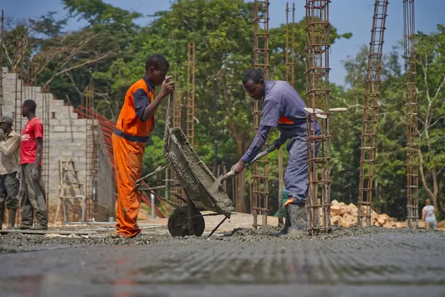 A crew pouring concrete with a wheelbarrow on a building site