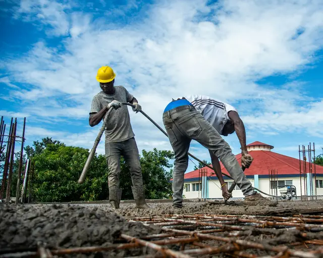 Two workers in hard hats spreading wet concrete over rebar