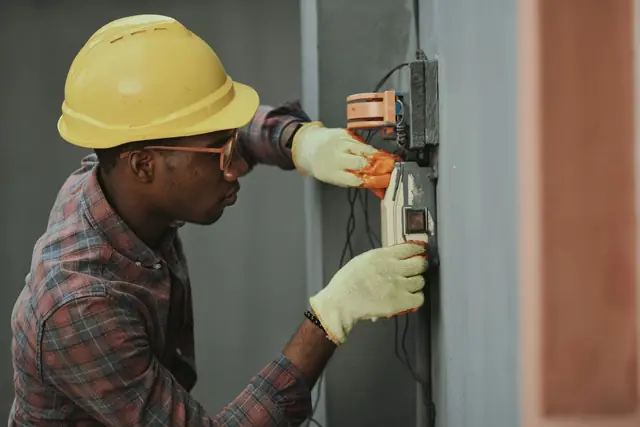 An electrician in a hard hat testing a panel