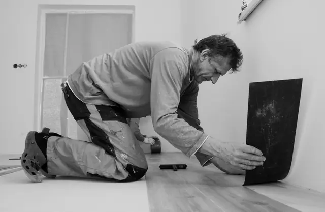 A flooring installer kneeling to lay a vinyl plank