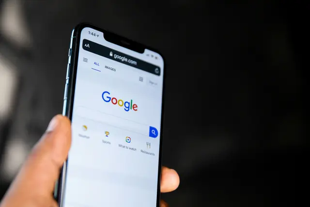 A hand holding a phone open to Google search