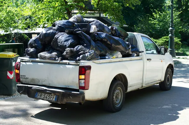 A white pickup truck loaded with black trash bags