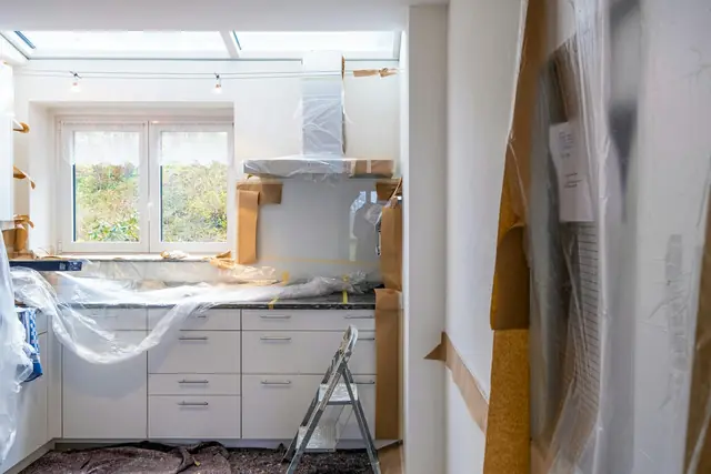 A kitchen in the middle of a renovation with cabinets covered in plastic