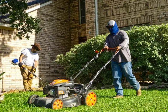 Two landscapers mowing and trimming a residential lawn