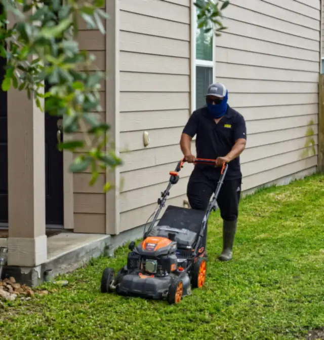 A landscaper mowing a lawn beside a house