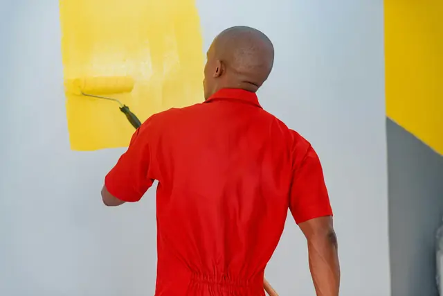 A painter in a red uniform rolling yellow paint onto a wall