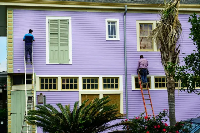 Two painters on ladders painting the front of a purple two-story house