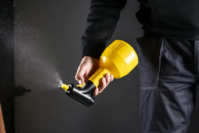 A technician in work clothes using a hand sprayer