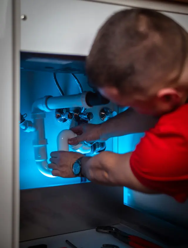 A plumber repairing pipes under a sink