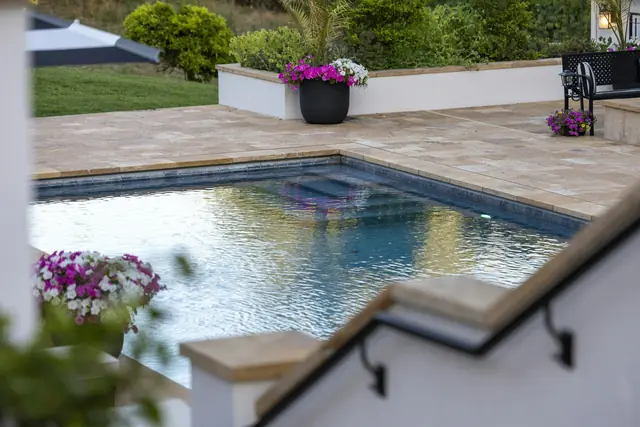 A backyard swimming pool with a stone patio and flowers