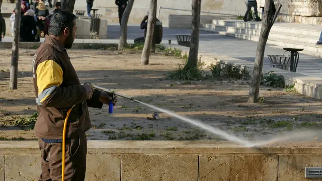 A worker spraying a stone walkway with a pressure washer