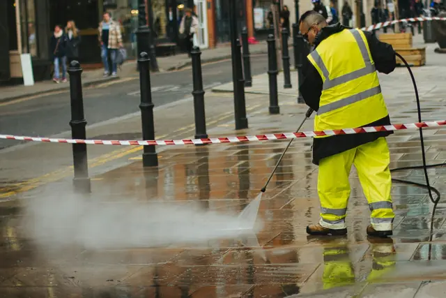 A worker in a high-visibility jacket pressure washing a street