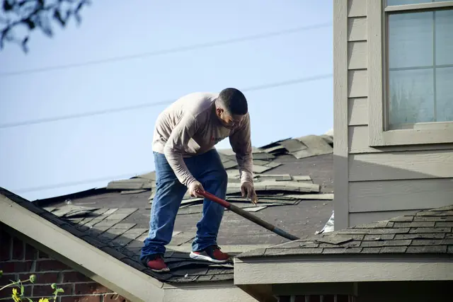 A roofer removing old shingles from a residential roof