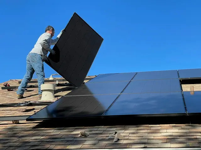 An installer setting a solar panel onto a shingled roof